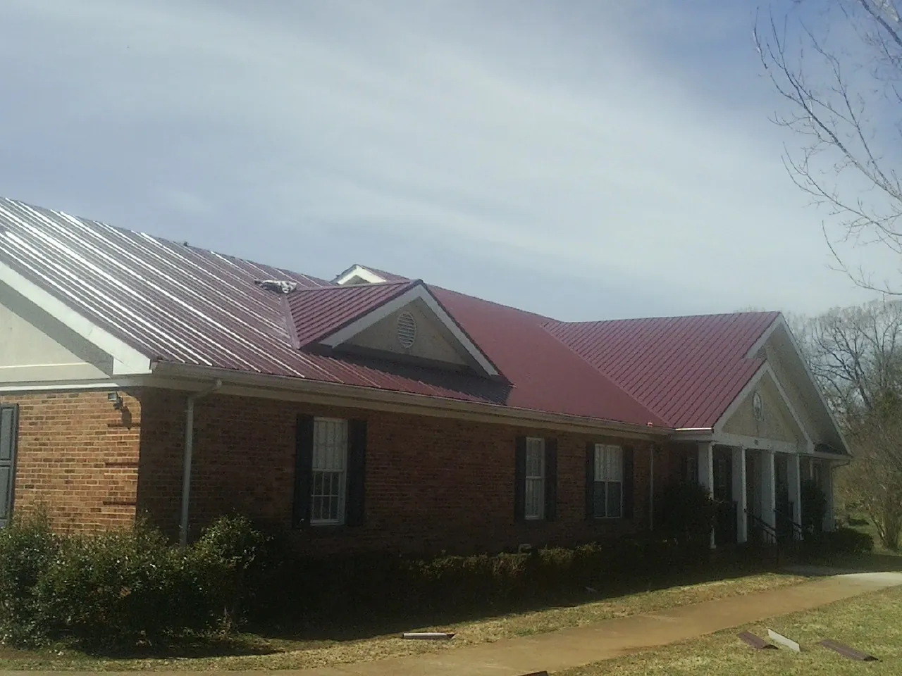 Red metal roof with gabled entries on a long brick building, from a Hail Damage Roof Repair job in Eagle Bridge