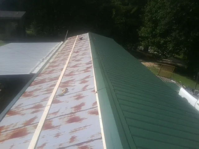 Old rusted panels beside newly installed green metal roofing — Wind Damage Roof Repair by Roofing Brothers in Eagle Bridge