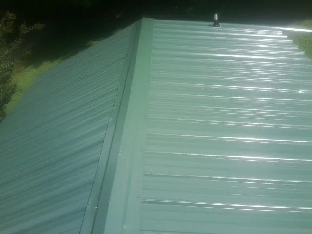 New green metal panels meeting at the ridge of a roof — Flat Roof Repair work by our crew in Eagle Bridge