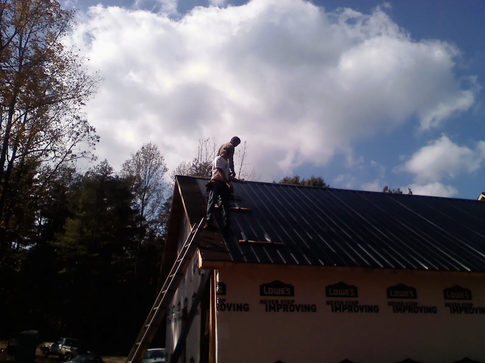 Roofer fastening dark metal panels high against a cloudy sky, from a Roof Inspection job in Eagle Bridge