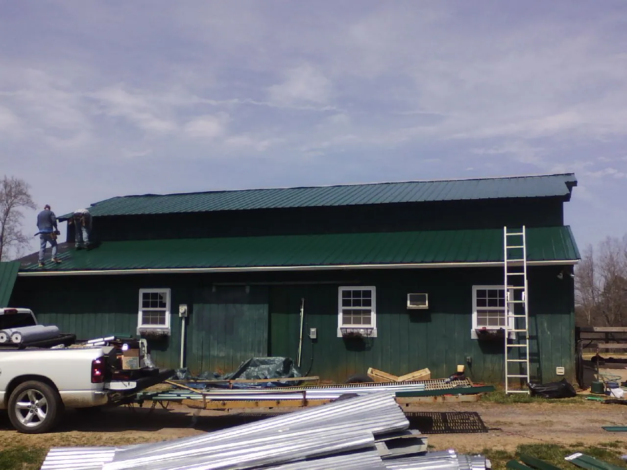 Crew installing green metal roofing on a large green barn in Eagle Bridge