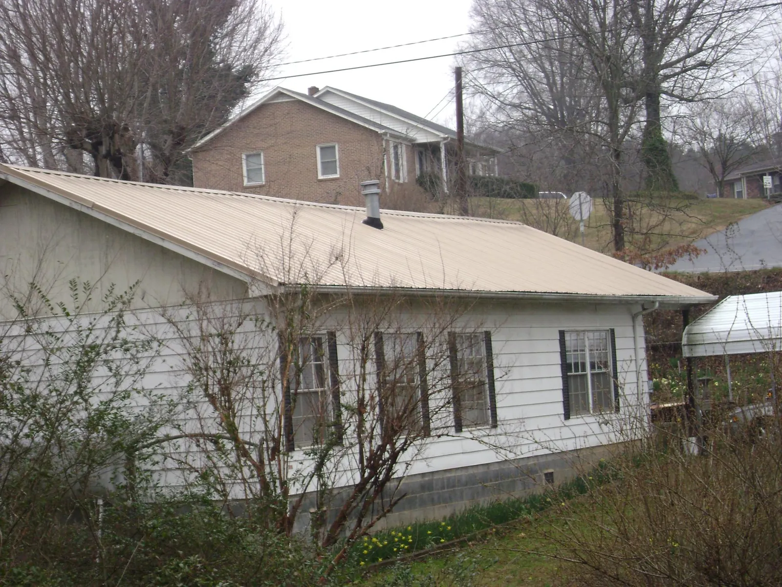 Tan metal roof on a white sided house set into a hillside — Commercial Roofing by Roofing Brothers in Eagle Bridge